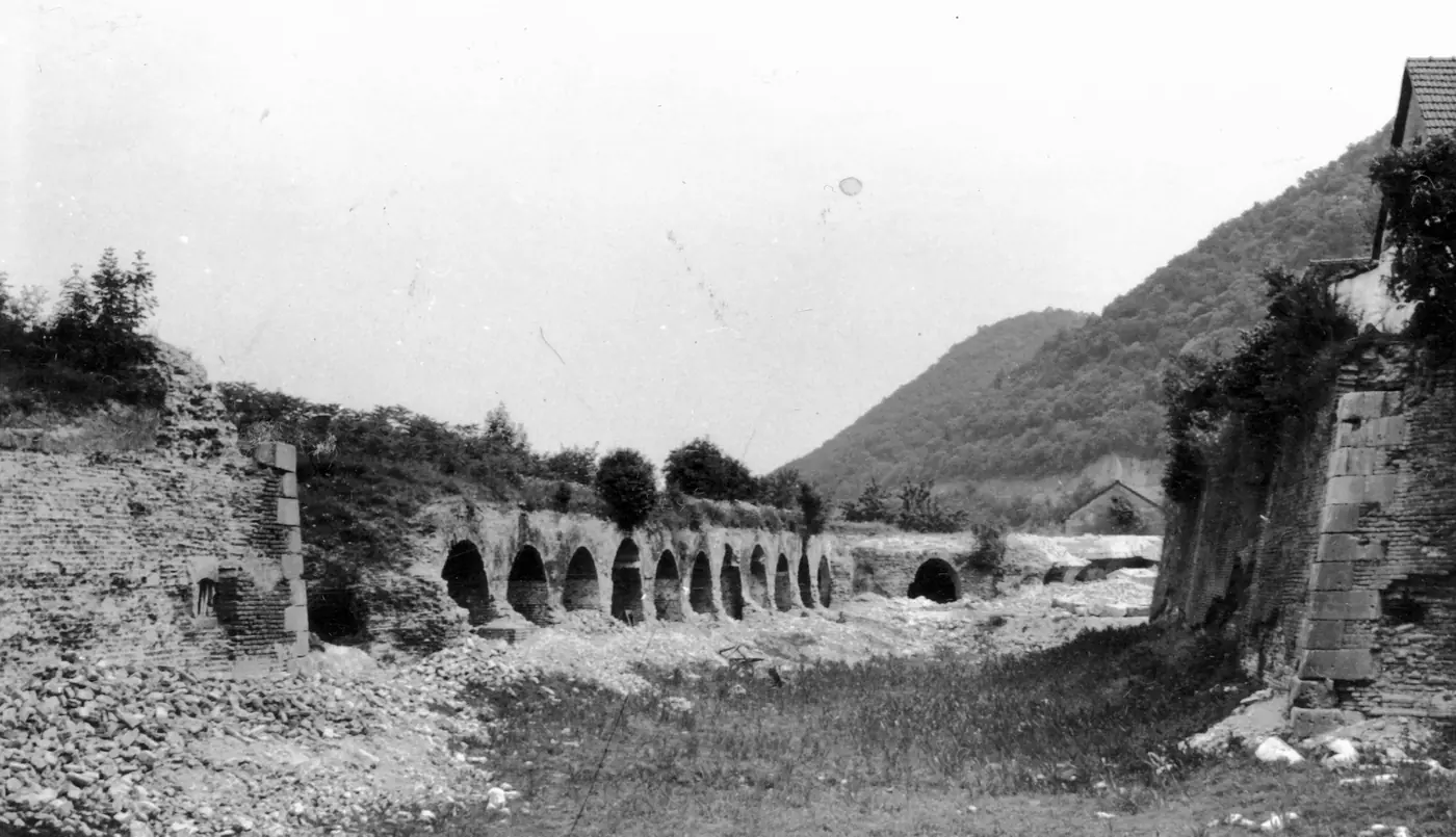 Fotografie alb-negru: șanțul cetății, uscat, cu un șir lung de arcade de cazemate și moloz.