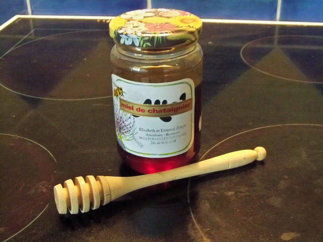 A pot of honey beside a wooden spoon