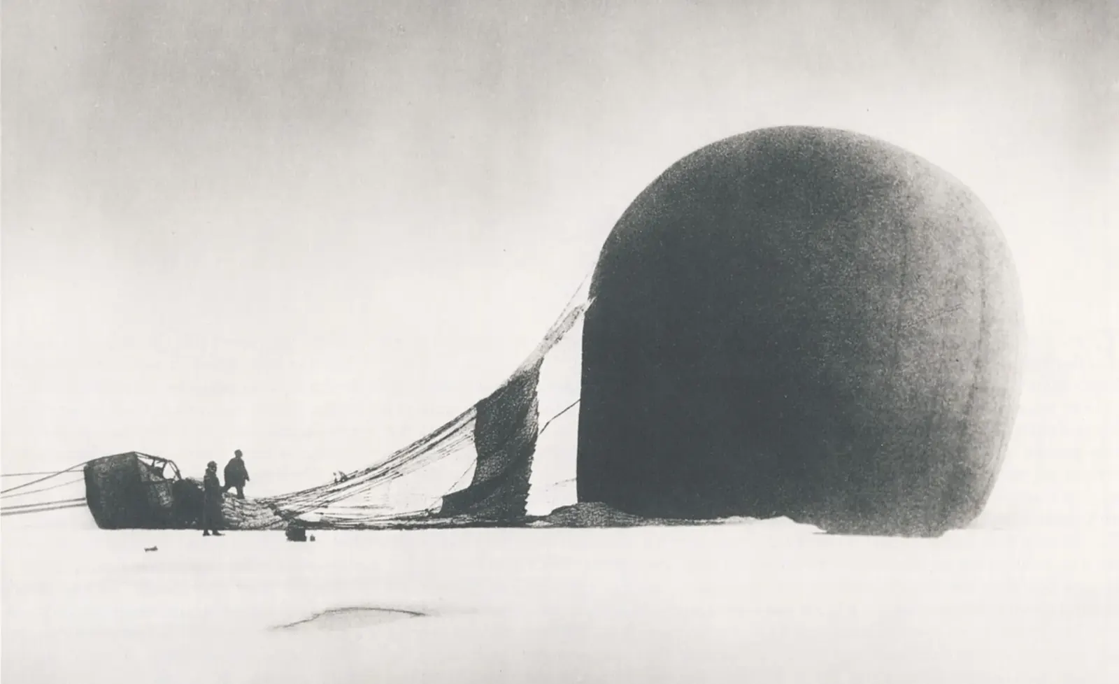 The half-deflated balloon lies on its side on the ice; beside the basket, two small figures. Everything is white and grey.