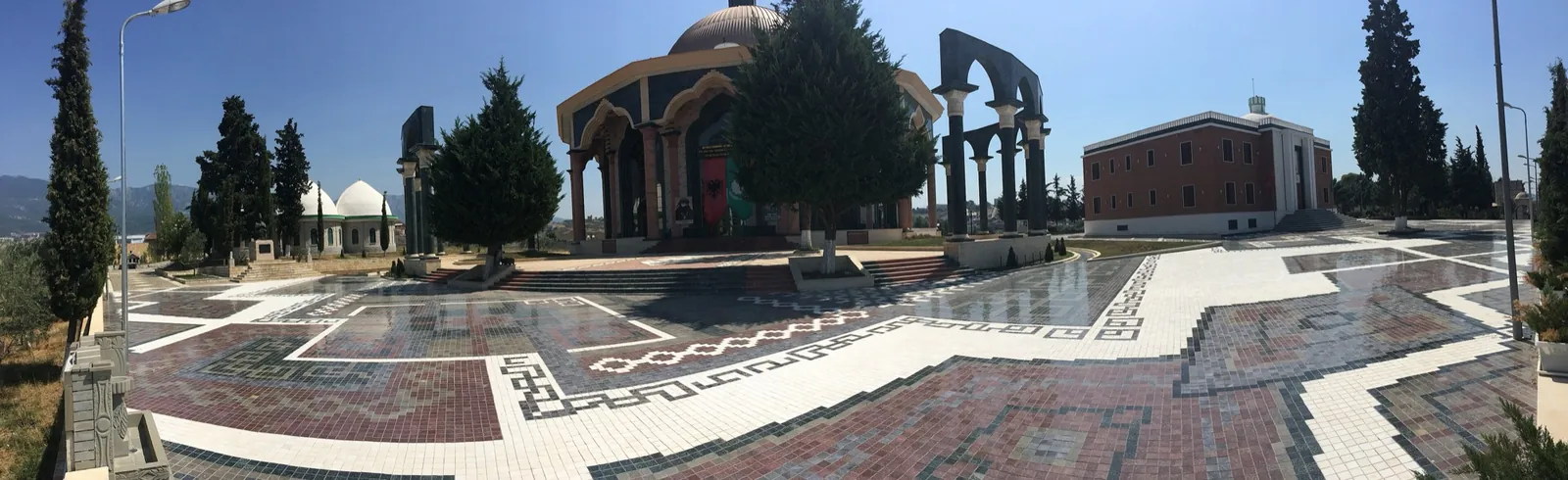 Panoramă a complexului Sediului Mondial Bektashi din Tirana: dale policrome, un pavilion cu cupolă și clădiri în fundal