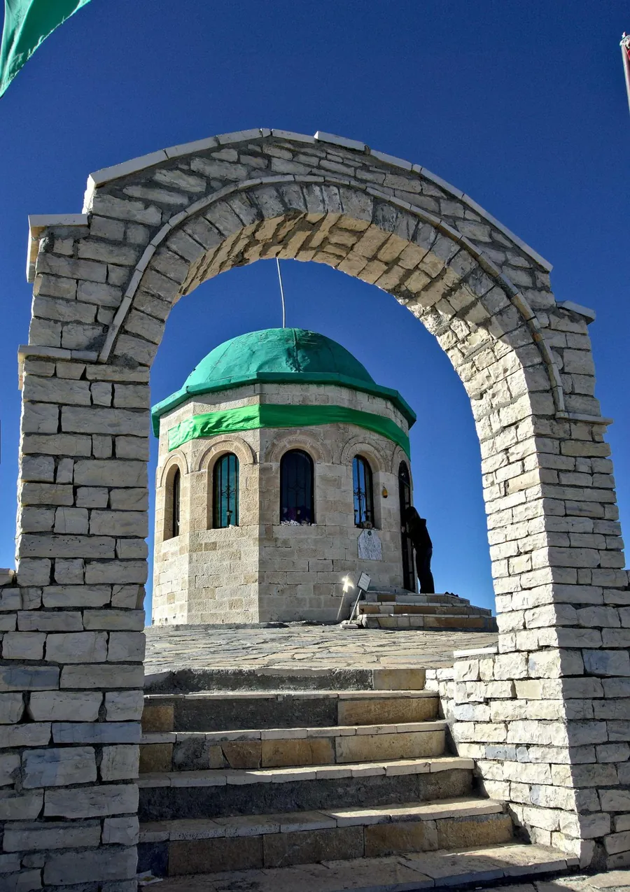 Un arc de piatră încadrând mausoleul cu cupolă verde de pe vârful Tomorr