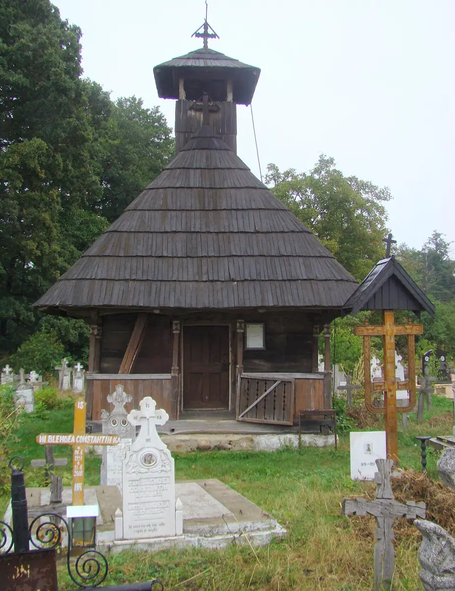 Biserica de lemn din Hobița, județul Gorj: clădire scundă cu pridvor deschis și acoperiș larg de șindrilă, într-un cimitir de sat.