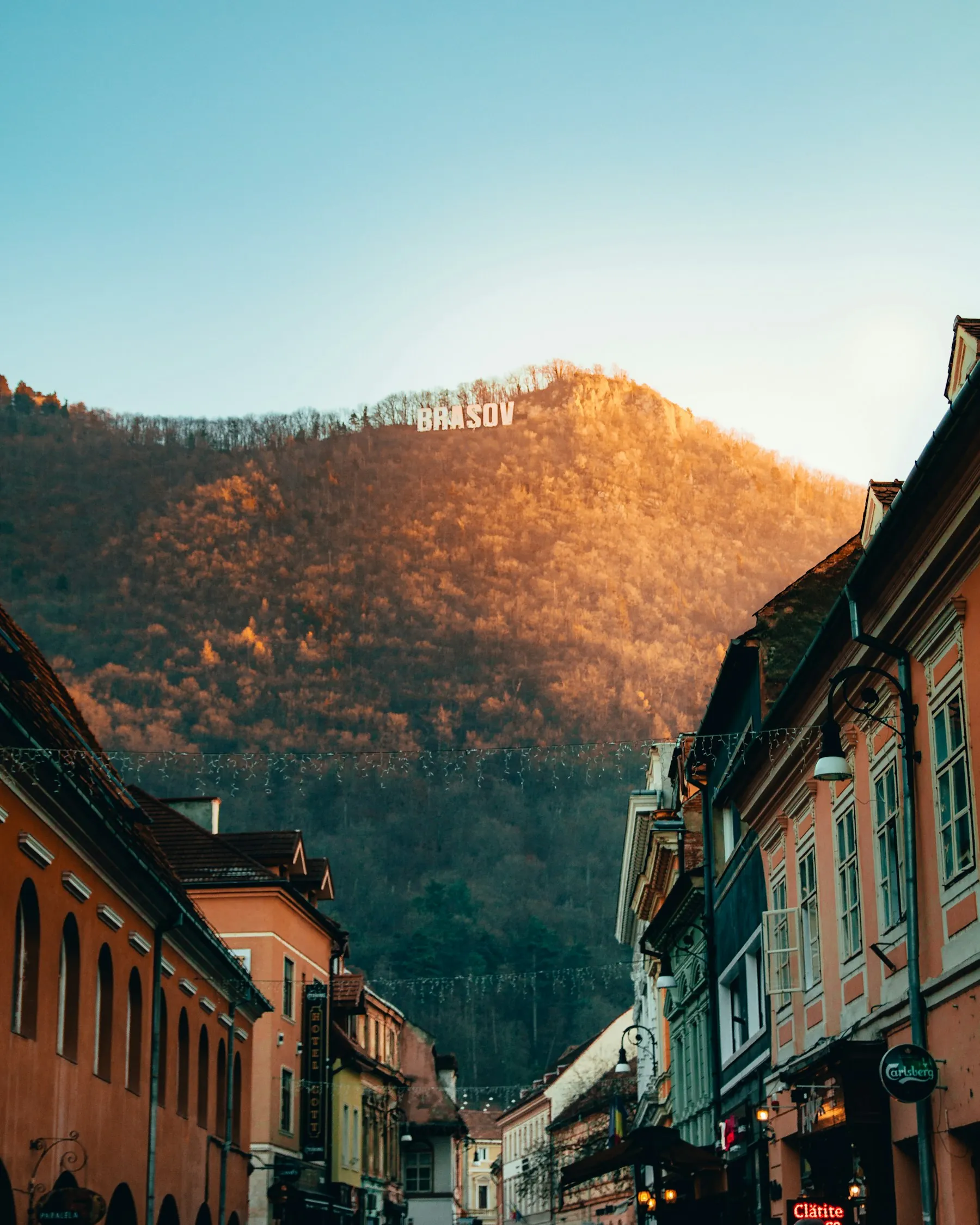 A narrow street with old houses, and at the end the mountain Tâmpa lit by the sunset, with the letters BRAȘOV