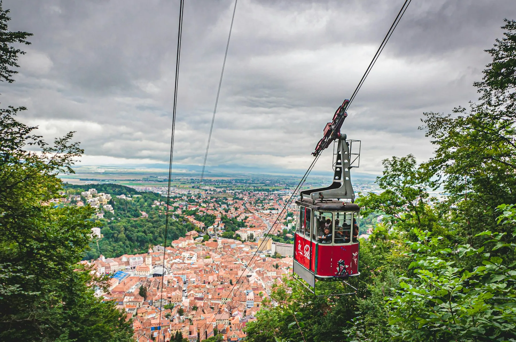A red cable-car cabin above the forest, with the city below