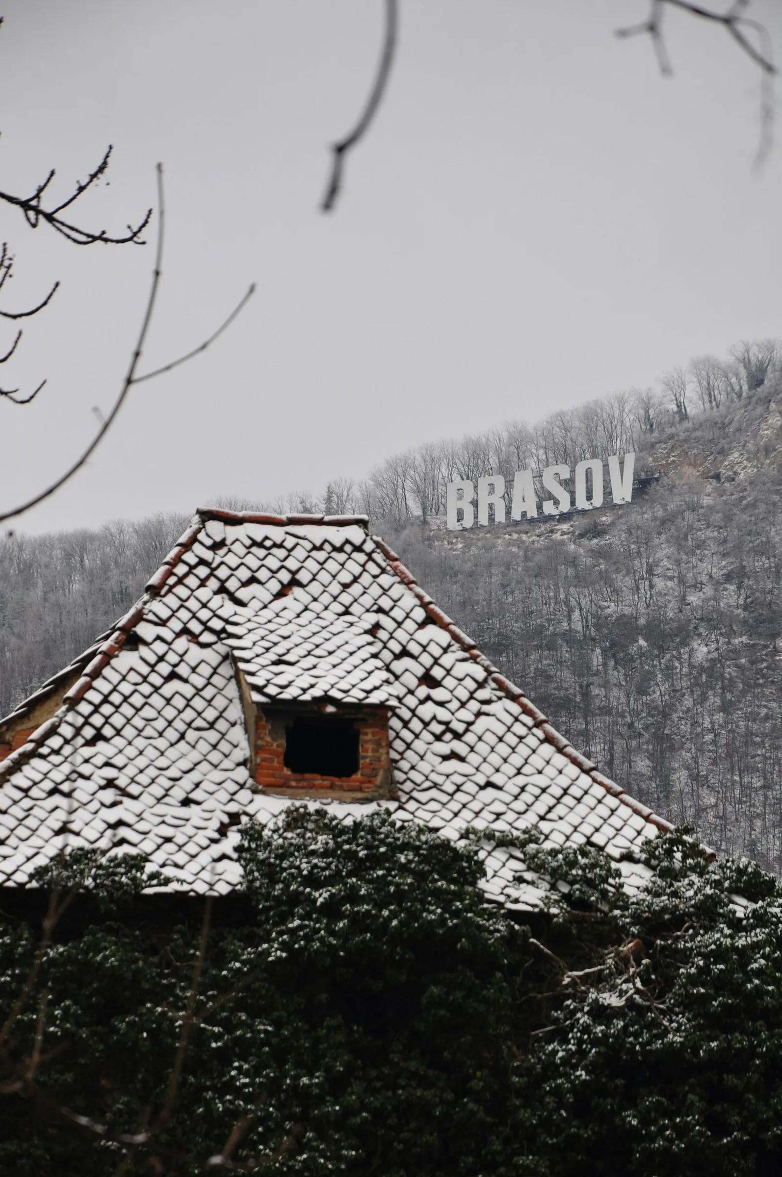 A tiled roof covered in snow, with the letters BRAȘOV on the hill behind