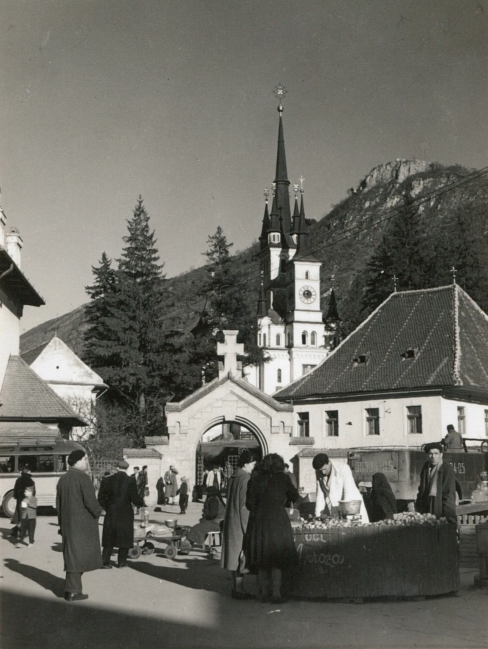 Black-and-white photograph: people at a market in front of a church with Gothic spires, with the hill behind