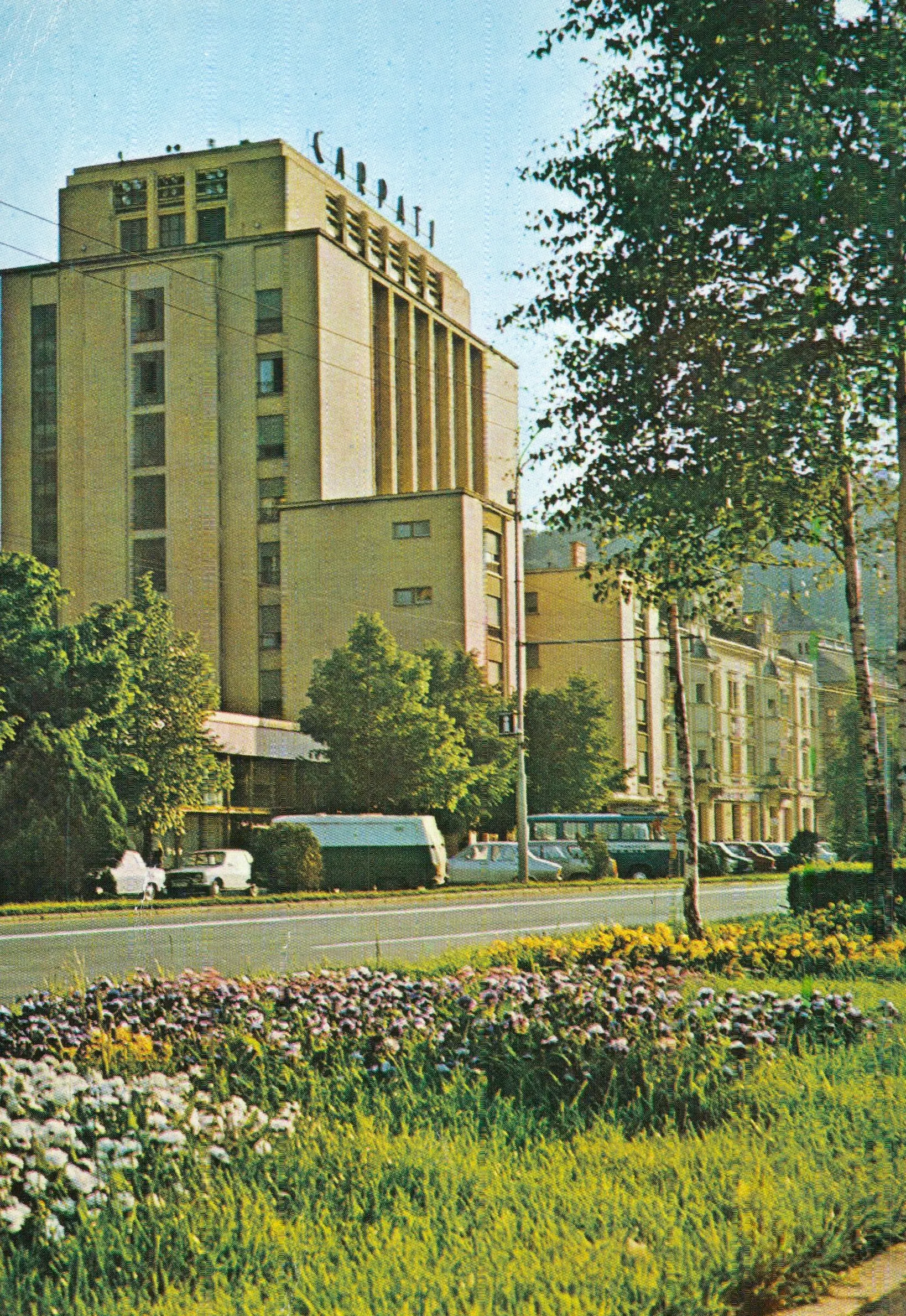 Colour postcard: a tall building with a yellow façade, with a street and flower beds in front