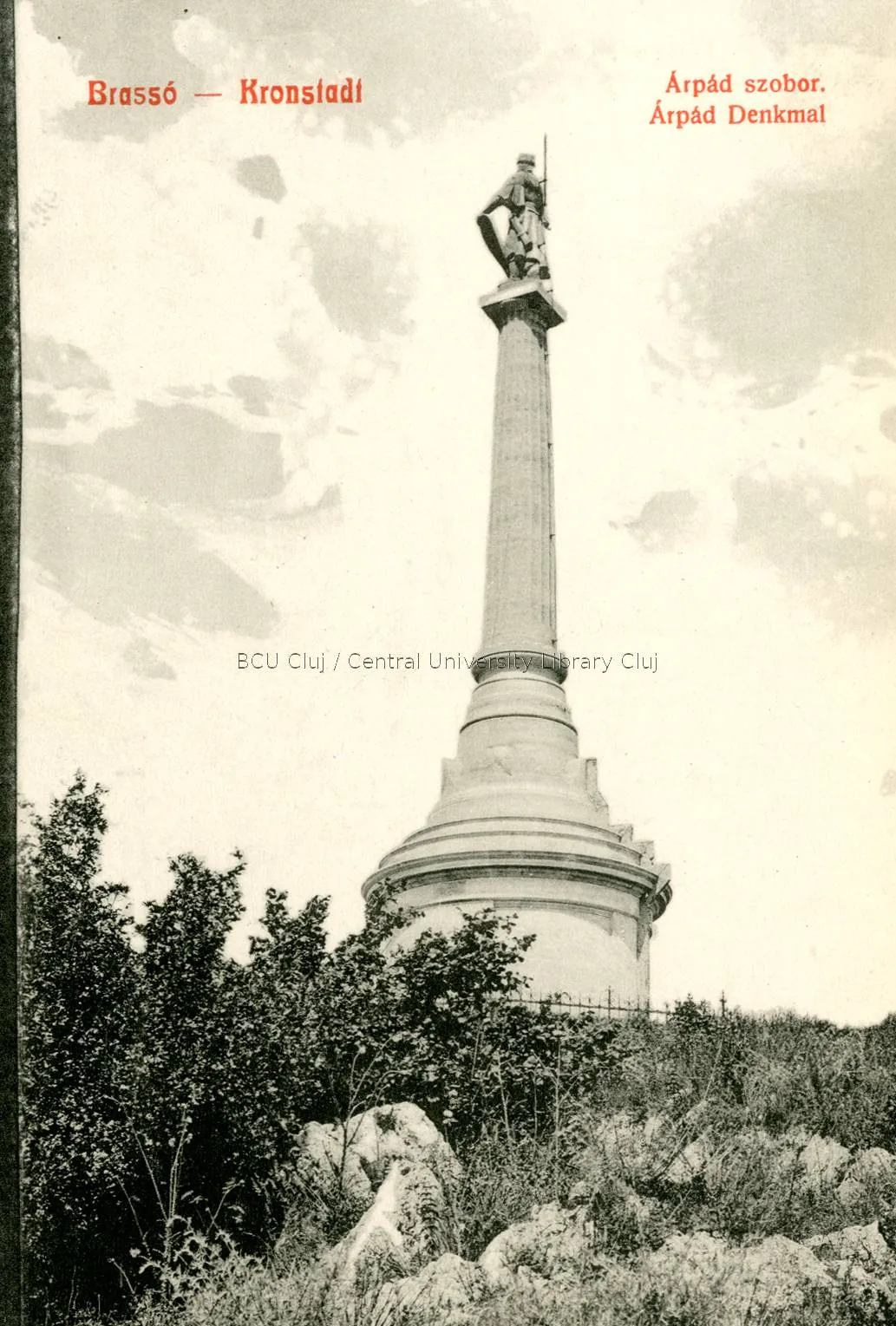 Black-and-white postcard: the column with a statue among rocks and fir trees