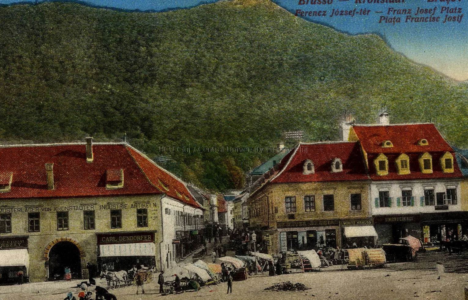 Colour postcard: houses with red roofs and dormer windows, in a square, with the wooded hill behind