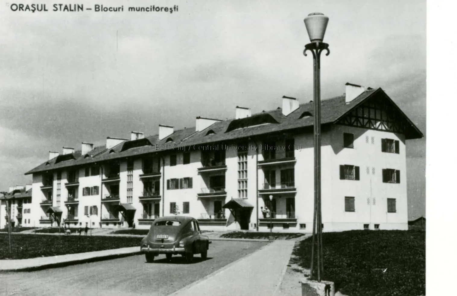 Black-and-white illustrated card: a three-storey block, a street lamp and a car in the street