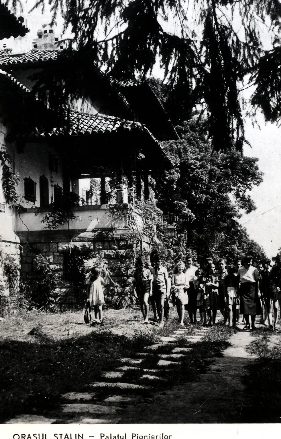 Black-and-white illustrated card: a building with a wooden roof among fir trees, with people on the path