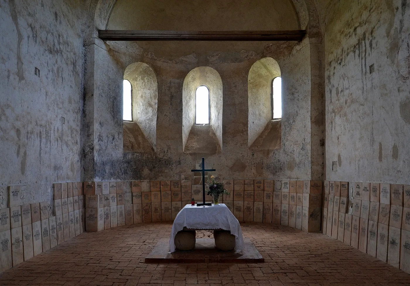 Interiorul bazilicii romanice din Cisnădioara: nava cu ziduri albe de piatră, trei ferestre înguste în absidă și un altar simplu.