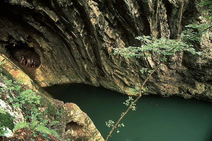 Lacul Dracului, un ochi de apă verde-închis sub un perete de calcar.