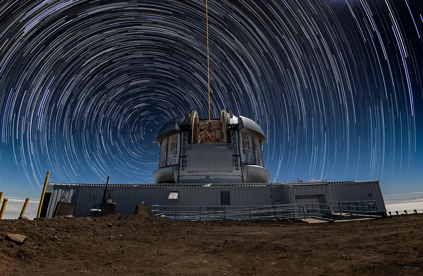 Long-exposure photograph: white star trails in concentric circles in the night sky, above a large telescope.