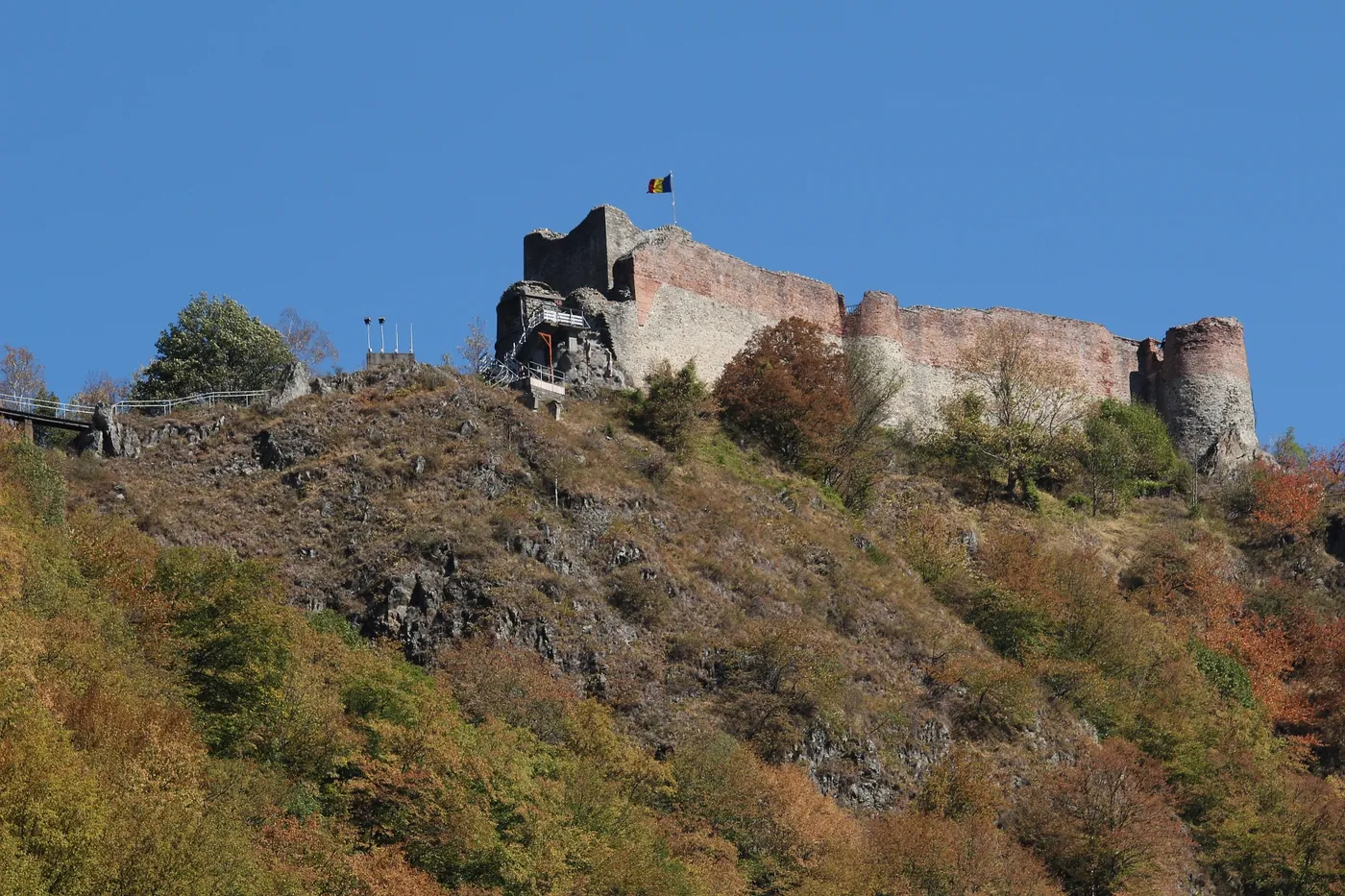 Poenari Fortress on the wooded ridge, with the Romanian flag.