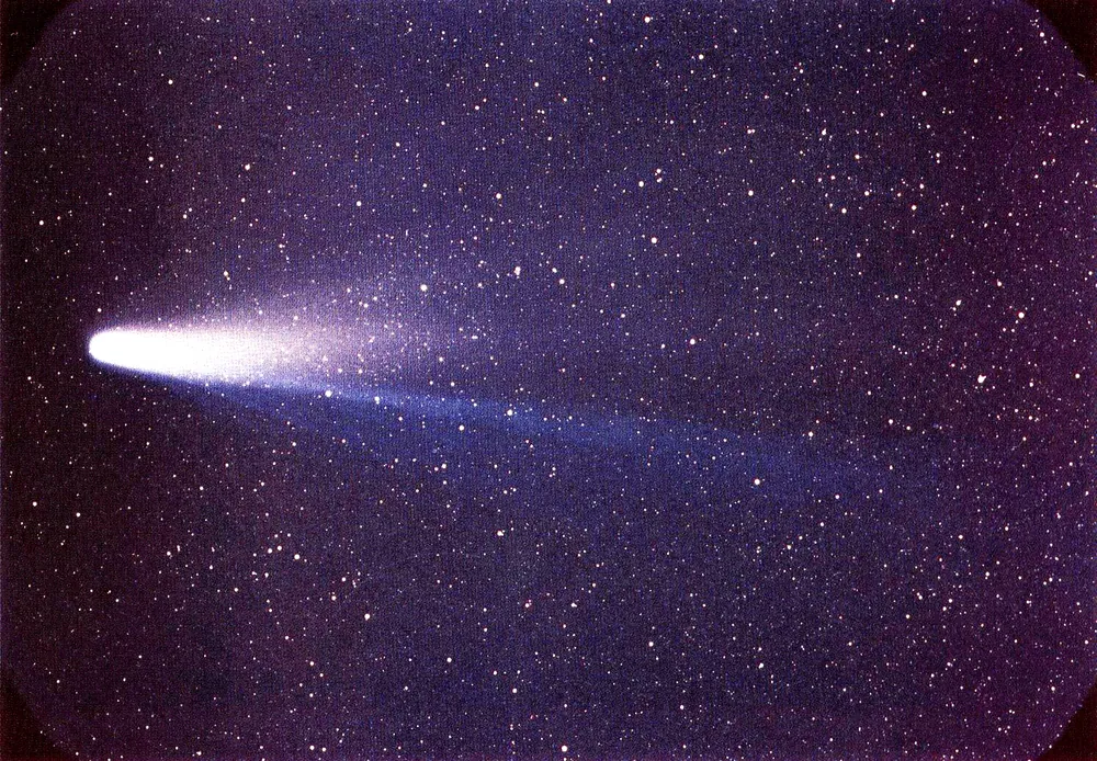 Photograph of a comet with a broad pale tail against stars.