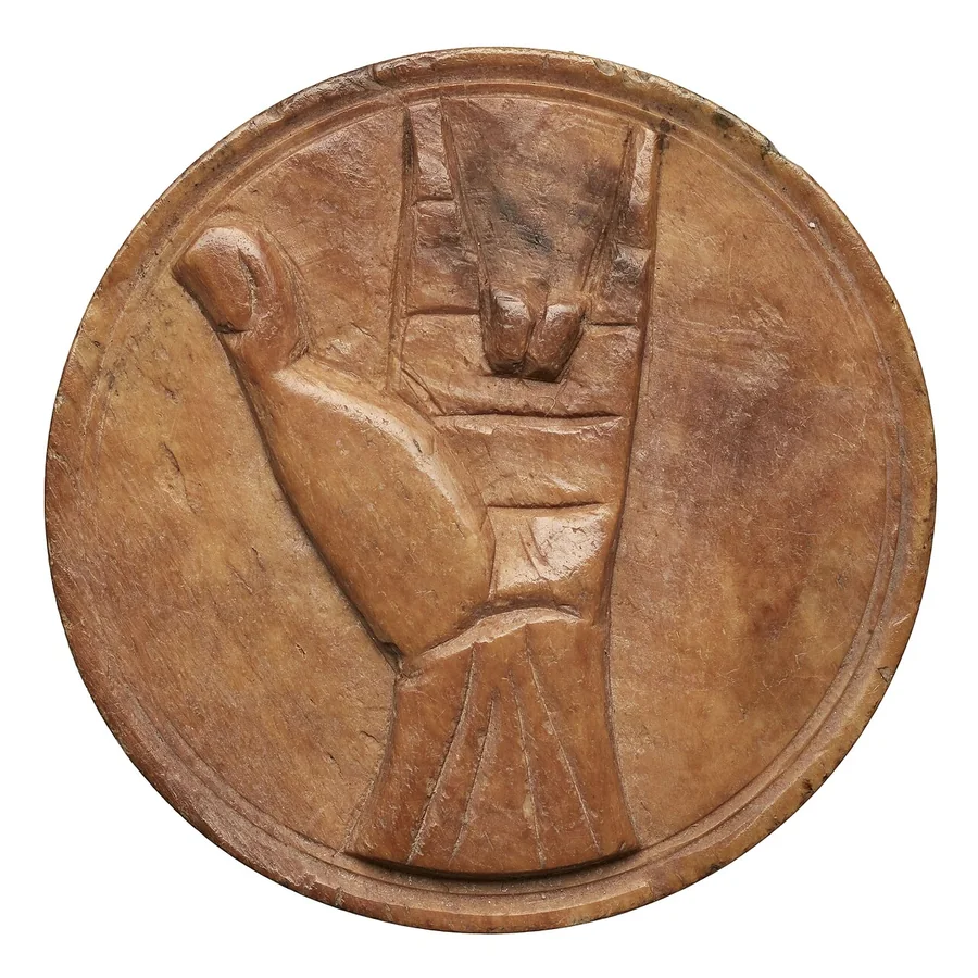A round ivory disc carved with a hand, two fingers bent.
