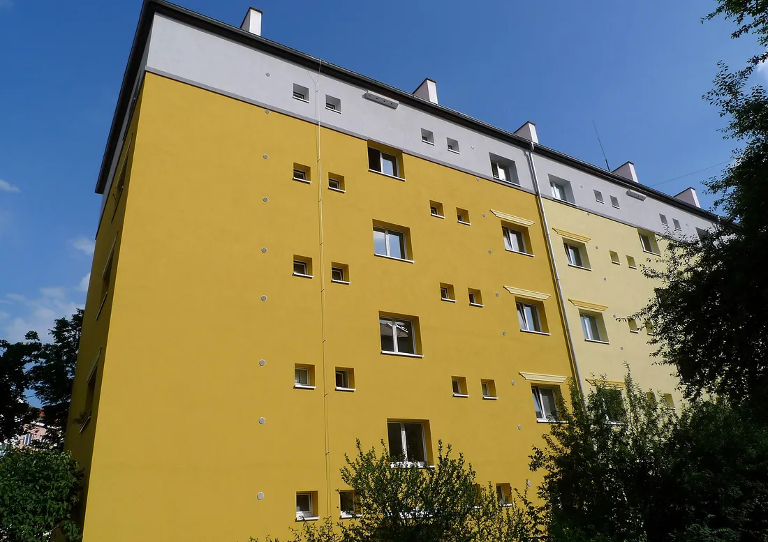 Un bloc cu cinci etaje, galben, cu șiruri de cutii mici de cuib montate sub ferestre și sub acoperiș.