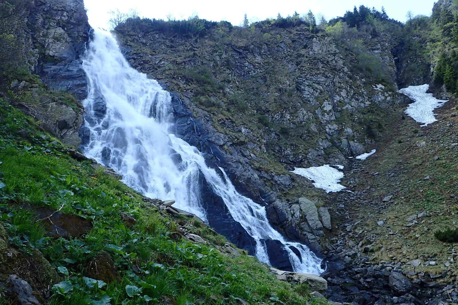 Cascada Bâlea curge peste stânci, lângă petice de zăpadă.