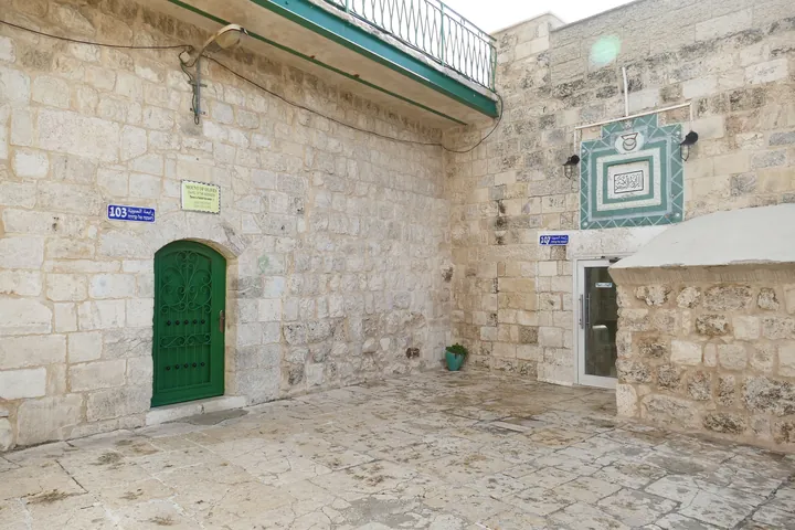A small octagonal stone chapel in a courtyard, with blind arches on its sides.
