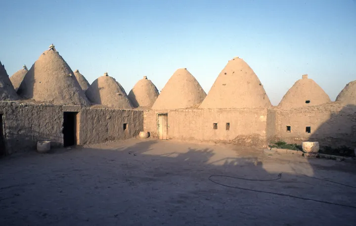 Mud-brick houses with conical roofs like beehives under a clear sky.