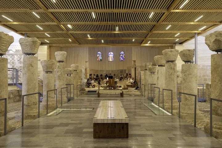 The interior of a modern basilica with a timber roof, over old mosaics and stone columns.