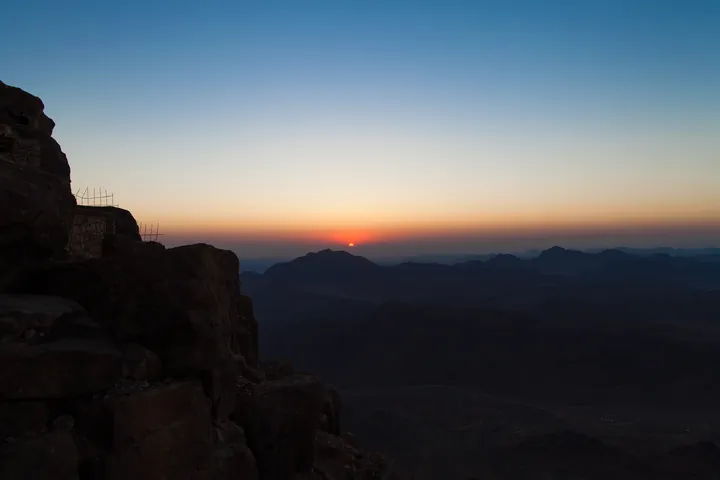 Ridges of reddish granite at sunrise, with mist in the valleys between them and an orange sky on the horizon.