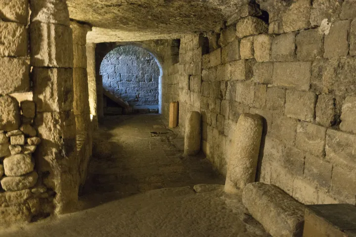 A ruined stone gallery with arches cut into the rock, grass growing on its floor.