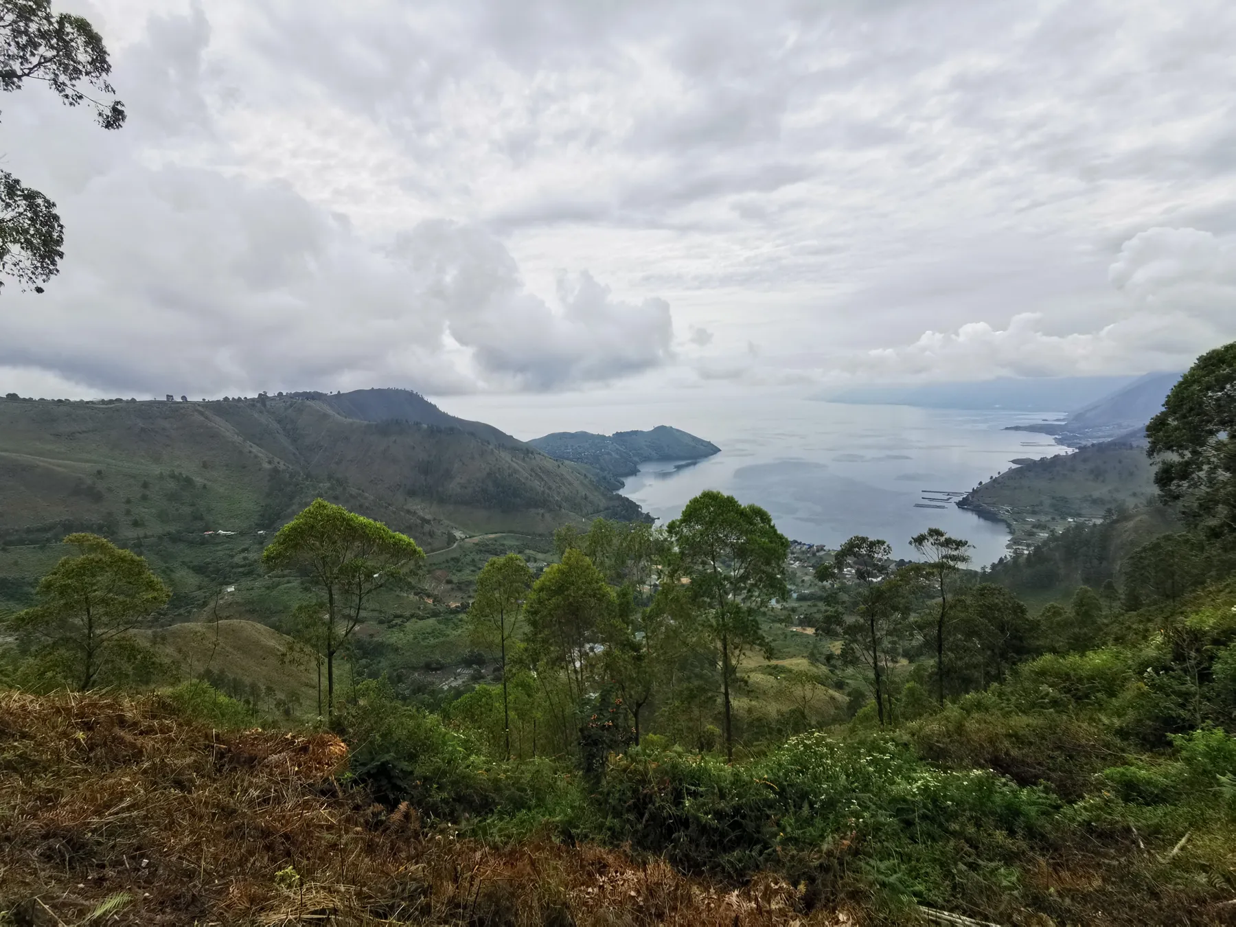 A wide lake between green mountains under cloud.