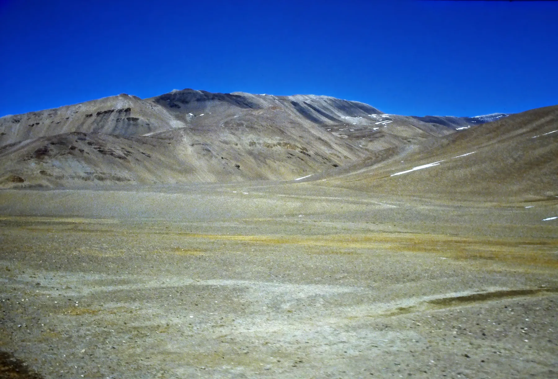 A bare high valley under bare mountains and blue sky.