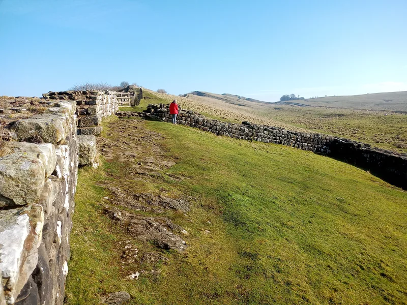 Hadrian's Wall on Cawfields Crags, with a walker on the path beside the Wall.