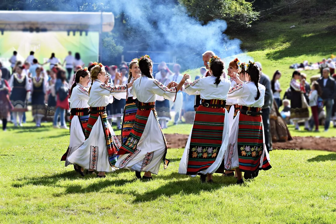 Bulgarians dancing the horo in folk costumes. Through the Bulgarian form the word entered Romanian.
