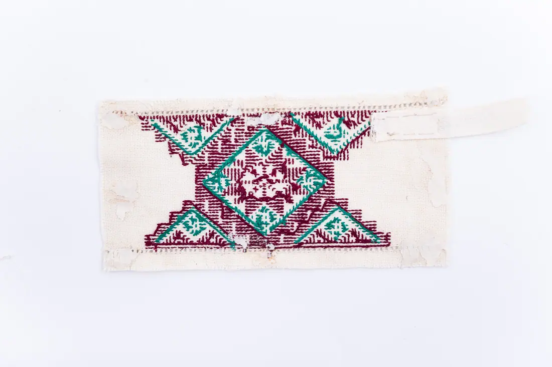 Fotografia muzeului: un model de broderie pe pânză albă, cu fir verde, vișiniu, cusut de David Katharina