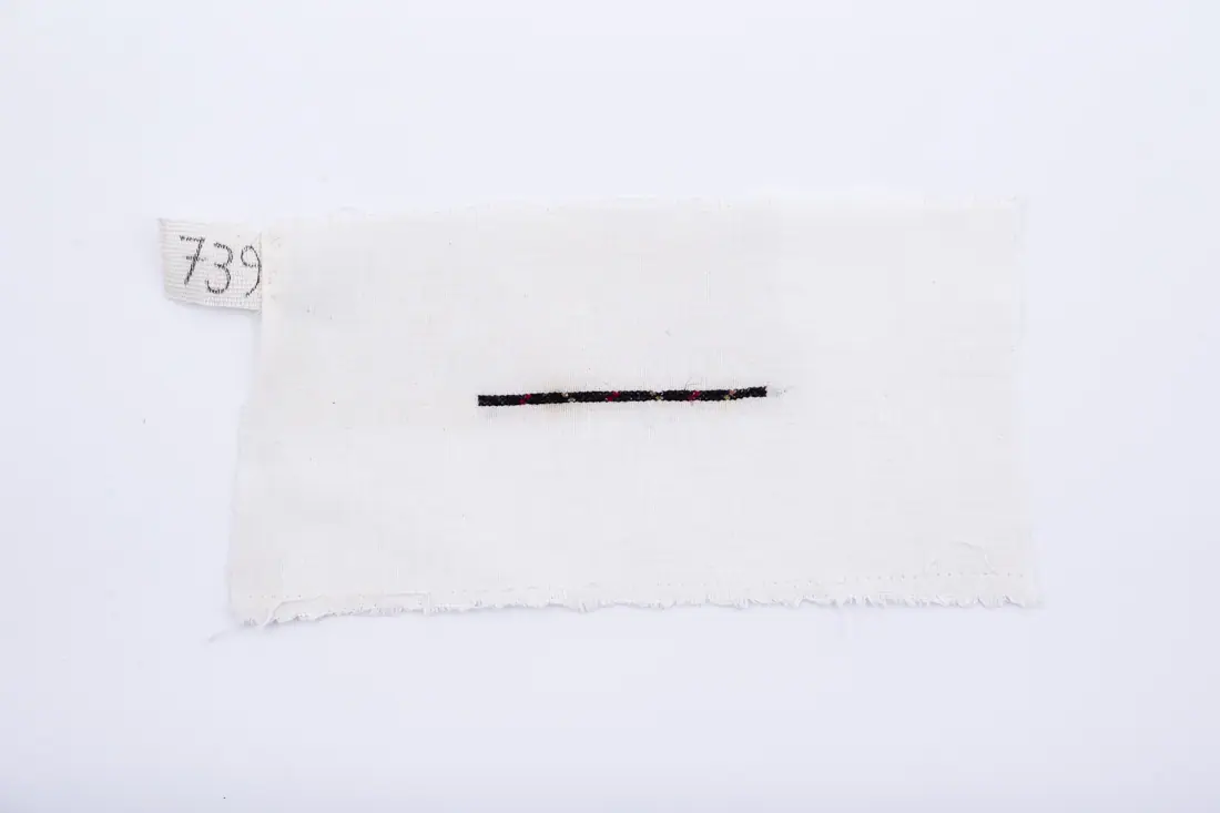 Fotografia muzeului: un model de broderie pe pânză albă, cu fir negru, roșu, auriu, cusut de Soră Mitrea Ciutană