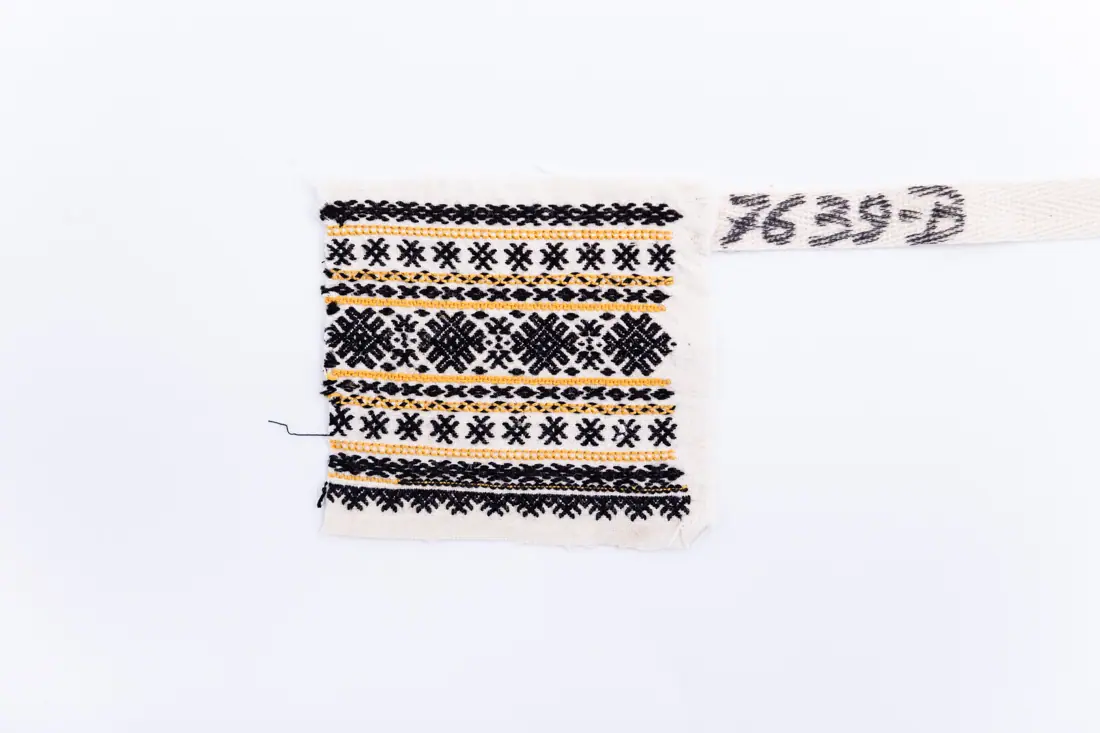 Fotografia muzeului: un model de broderie pe pânză albă, cu fir galben, negru, cusut de Stan Foarea
