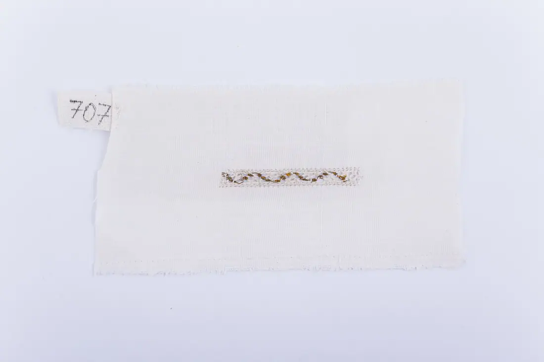 Fotografia muzeului: un model de broderie pe pânză albă, cu fir negru, galben, cusut de Soră Mitrea Ciutană
