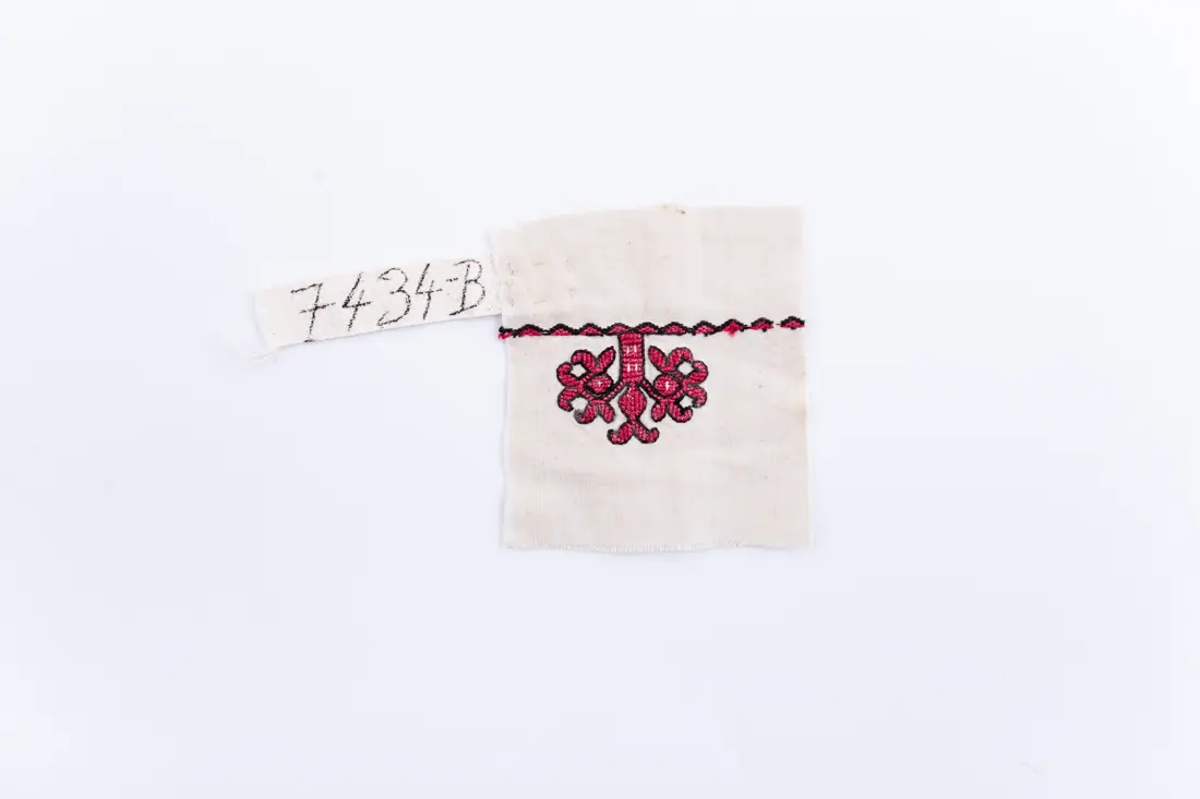 Fotografia muzeului: un model de broderie pe pânză albă, cu fir negru, roșu, cusut de Vlad Ana