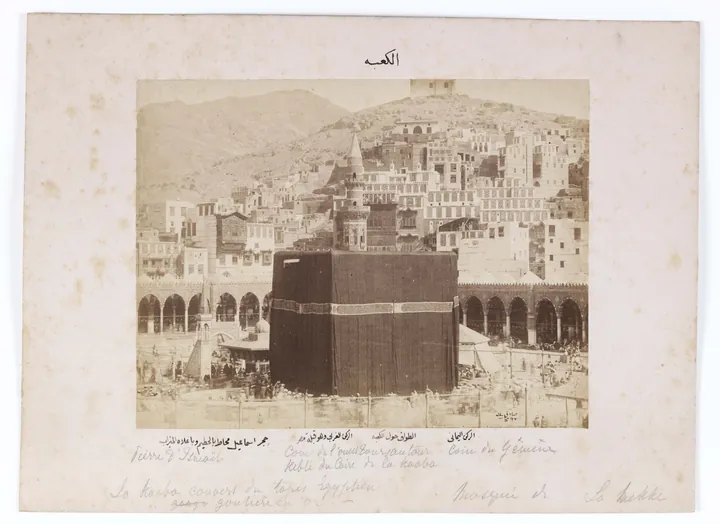 An early sepia photograph: the Kaaba draped in black cloth in the sanctuary courtyard, with stone houses behind.