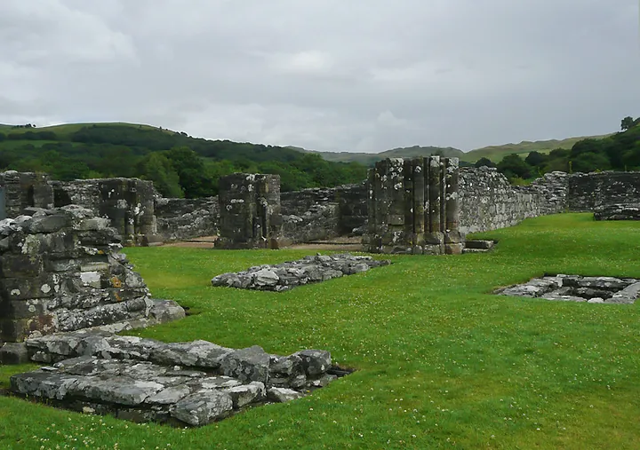 Colour photograph of roofless ruined stone walls standing in a green valley ringed by hills