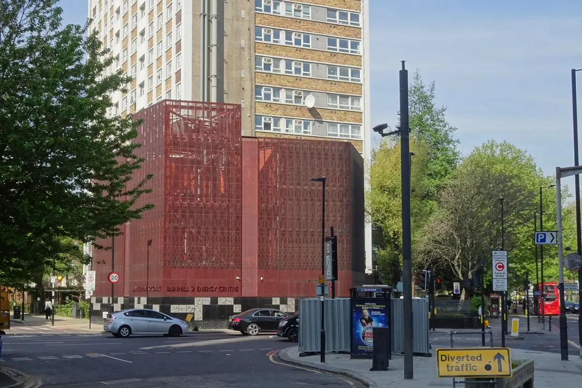 A red lattice building at a street corner in front of a tower block: the energy centre on the City Road station site.