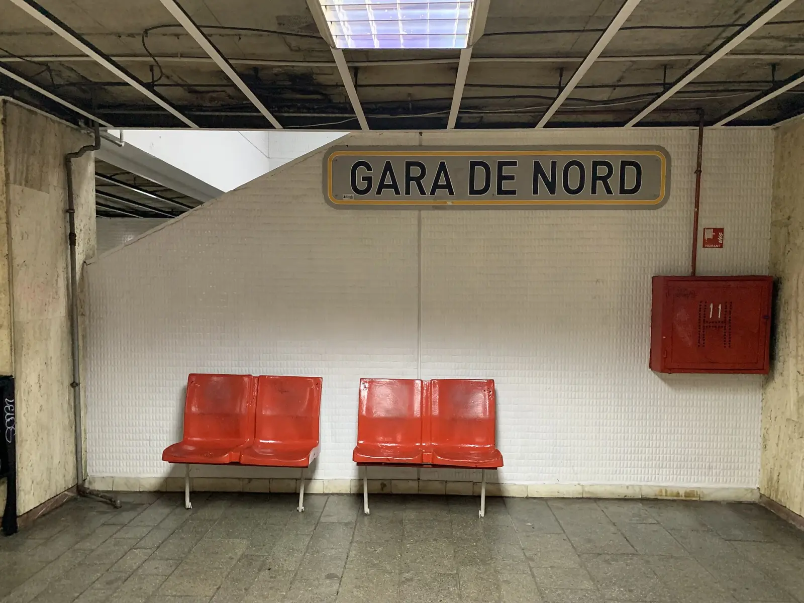 Peretele peronului cu numele stației și scaune roșii la Gara de Nord