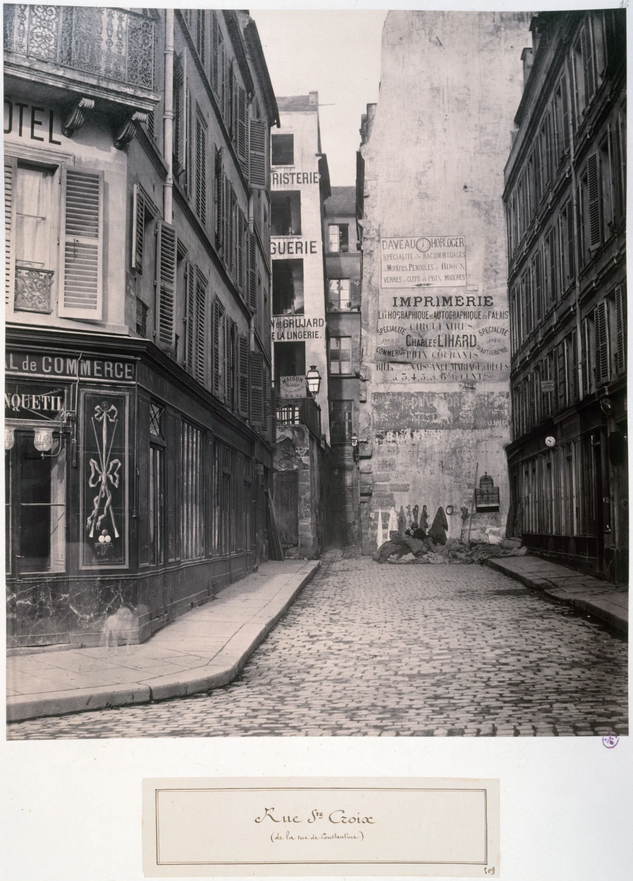 A narrow street between shopfronts, ending at a transverse building; the label identifies rue Sainte-Croix.