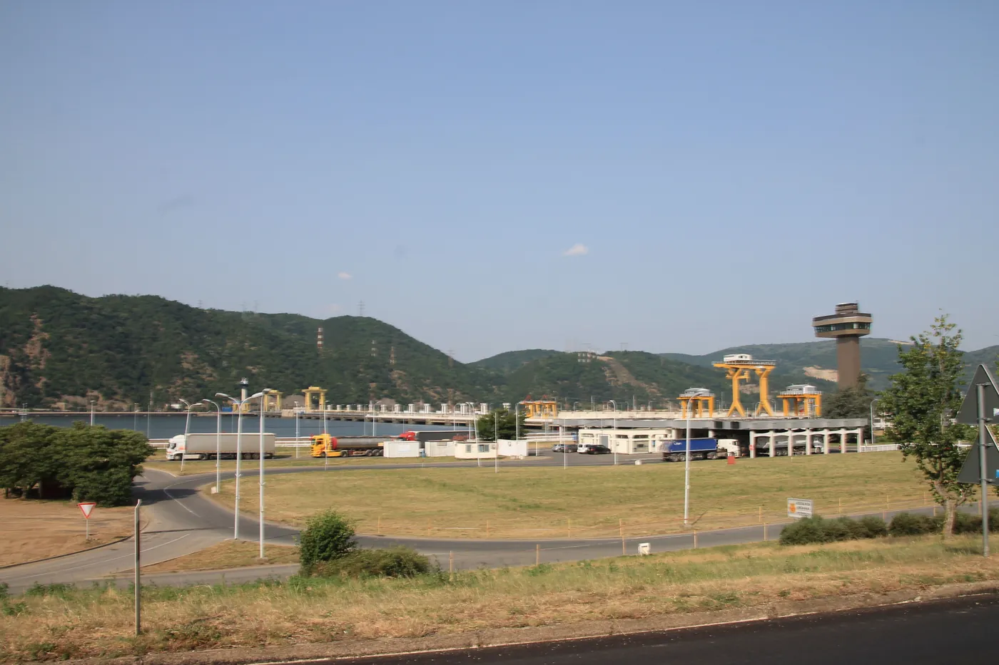 Barajul Porțile de Fier I: zidul de beton cu macarale galbene și turnul de control.