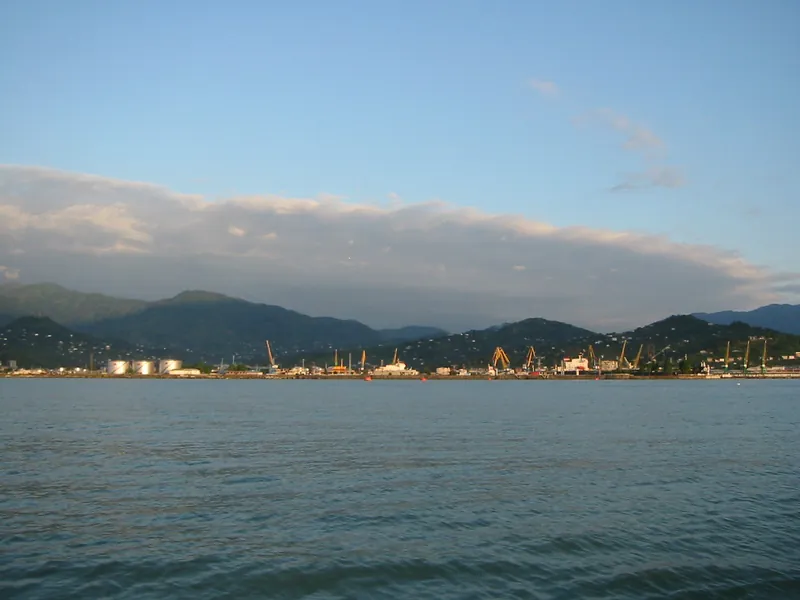 A low port with cranes at the foot of mountains, seen from the water