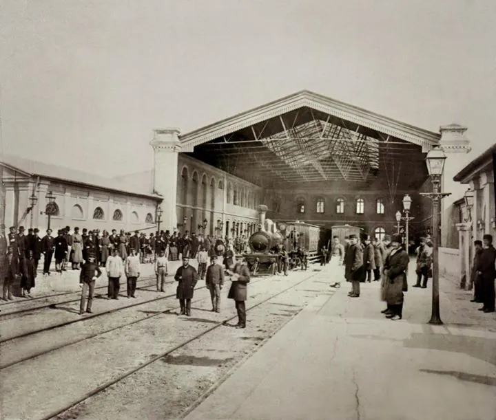 Interiorul Gării Filaret, cu hala acoperită, locomotivă și oameni pe peron.