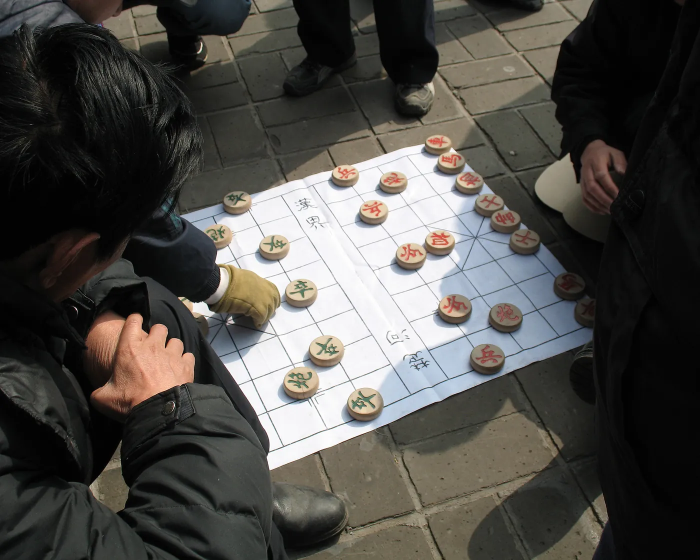 几个人蹲在人行道上围着一张象棋盘,其中一人伸手去走子。
