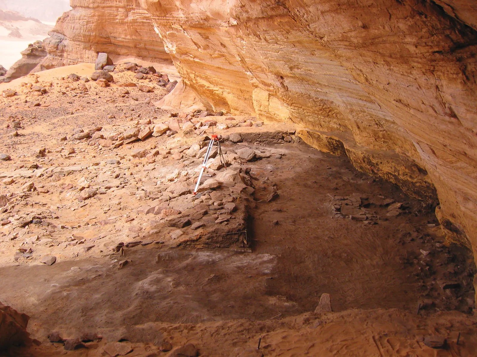 A sandstone rock shelter in the Acacus Mountains of Libya seen from the south, with a dry valley in front.