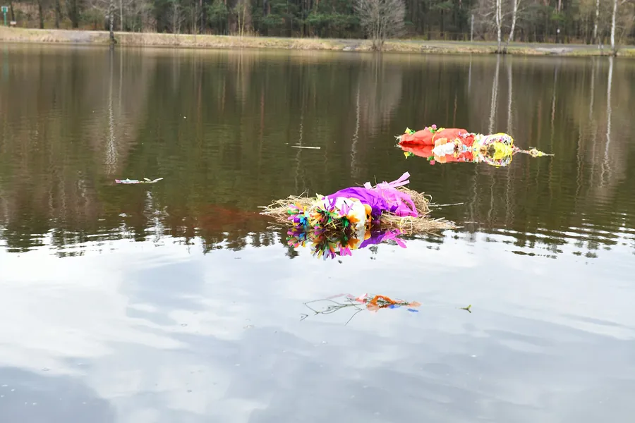 Two effigies dressed in bright cloth and flowers float on a lake.
