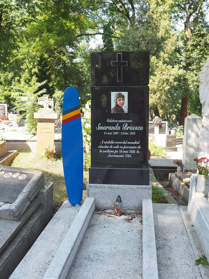 Black grave monument in the Cluj cemetery bearing the flyer's portrait, a blue propeller beside it, and the years 1897–1948.