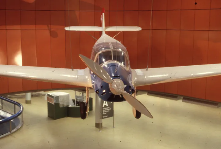Blue-and-white Messerschmitt Bf 108 hanging from a museum ceiling, seen head-on.
